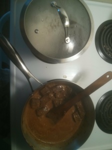 Beef rendang, still cooking down, next to a pot of rice cooking
